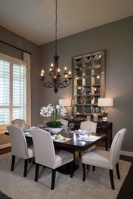 a stylish and exquisite taupe dining room with a dark stained table and a credenza, neutral chairs, a black vintage chandelier and a mirror piece on the wall