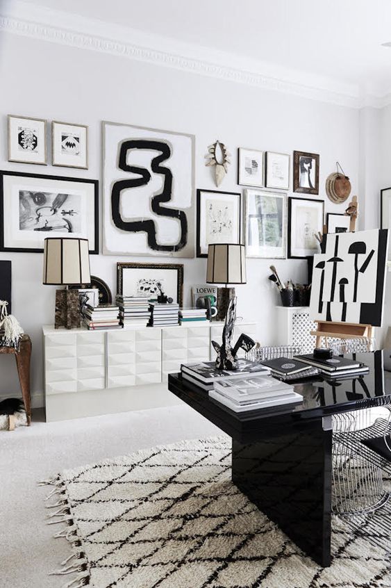 a stylish black and white home office with a polished black desk, a white storage unit, a monochromatic gallery wall and some table lamps
