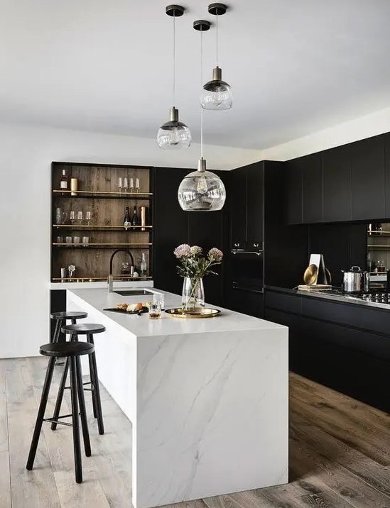 a stylish contrasting kitchen with sleek black cabinets, a white stone kitchen island, built in shelves and a cluster of pendant lamps