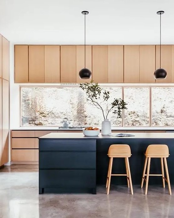a stylish light stained kitchen with a large window backsplash, a navy kitchen island, black pendant lamps and tall stained stools is perfection