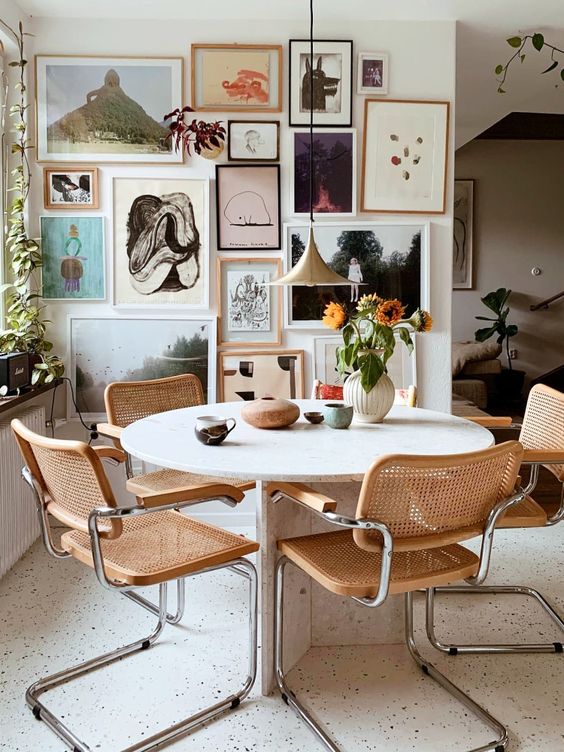 a stylish mid century modern dining room with a round stone table, cane chairs, a lovely gallery wall and a pendant lamp