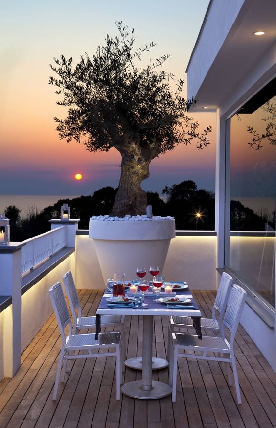a stylish modern balcony with white metal dining furniture, a large planter filled with pebbles, some lights and a cool sea view
