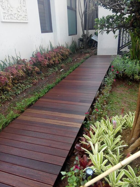 a stylish rich stained wooden walkway lined up with greenery and colorful foliage is a gerat idea for a chic modern space, it looks bold