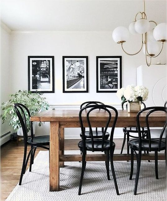 a stylish vintage dining room with a stained table and black chairs, a black and white mini gallery wall and potted plants and blooms