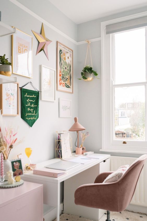 a sweet girlish home office with grey walls, a lovely gallery wlal, a white desk and a pink cabinet, a dusty pink chair and gold touches