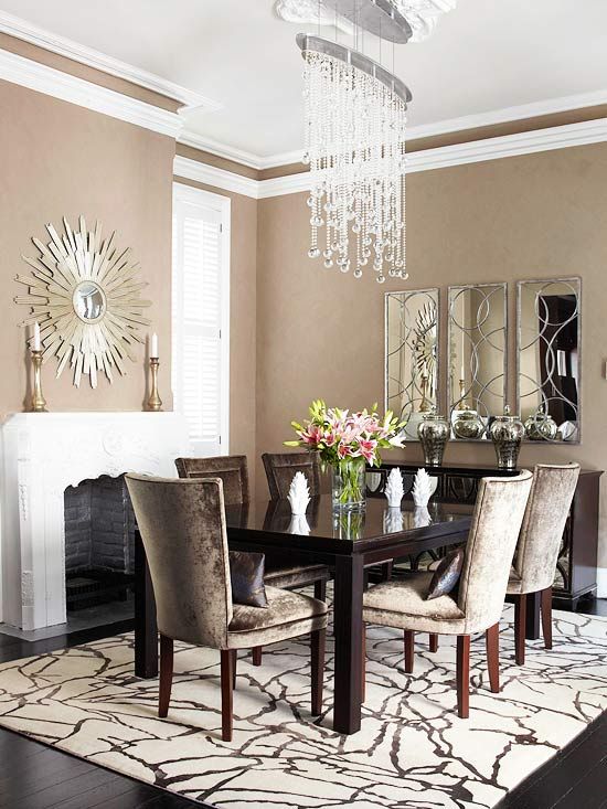 a taupe living room with a non-working fireplac,e a black table, taupe chairs, a chic crystal chandelier and a mirror of three parts