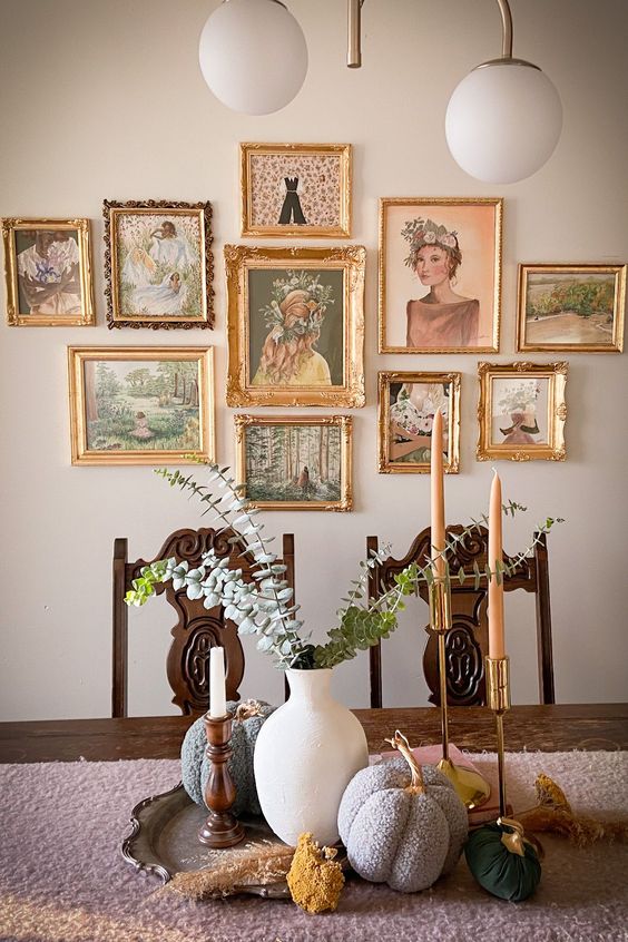 a vintage dining room with a dark stained table and chairs, a chandelier and some pumpkins and a beautiful gallery wall with gold frames