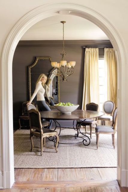 a vintage-inspired taupe dining room with a round table, vintage neutral chairs, a chandelier and a large mirror
