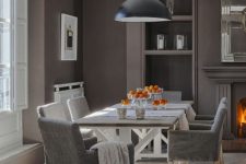 a vintage-inspired taupe dining room with a window in an alcove, built-in shelves, a fireplace, a trestle dining table and grey chairs