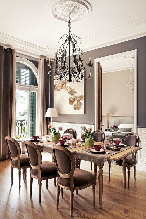 a vintage-inspired taupe dining zone with creamy paneling, a vintage table and taupe chairs, a chic chandelier and some art plus shutters on the window