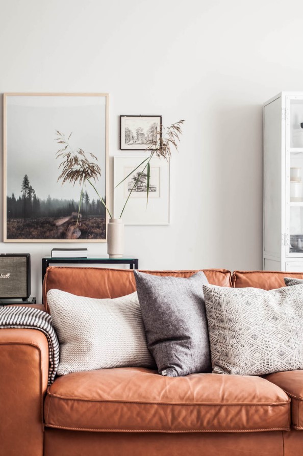 a welcoming living room with an amber leather sofa, neutral pillows, a mini gallery wall, a console table and some grasses