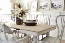 a white shabby chic dining room with a vintage table, loveseat and chairs, a ledge gallery wall with neutral landscapes and a vintage chandelier