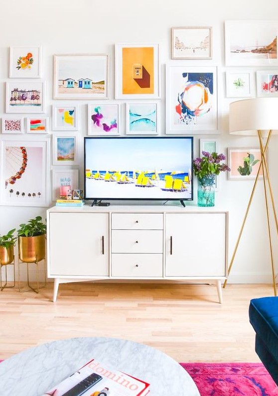 an airy and cool gallery wall with bright prints and watercolors and white frames includes a TV and makes the space bolder
