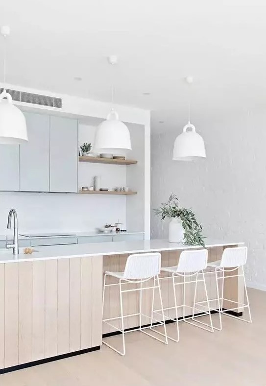 an airy coastal kitchen with light blue cabinetry, a large wooden kitchen island, white pendant lamps, white wicker stools