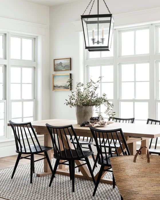 an airy vintage dining room with a stained table, black chairs, a pendant lamp on chain and a mini gallery wall