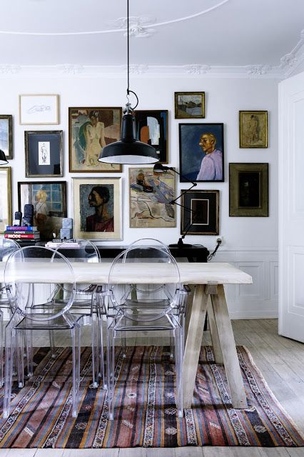 an eclectic dining space with a trestle table, ghost chairs, a black console table and a vintage gallery wall plus a boho rug
