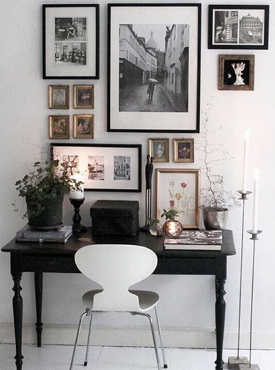 an eclectic home office with a black vintage desk, a white chair, a monochromatic gallery wall and potted greenery and candles
