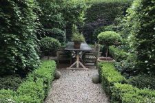 an elegant and chic garden with lots of greenery and green trees, with potted plants and stone spheres is amazing