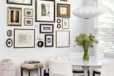 an elegant dining room with a round table and creamy chairs, a pendant lamp and a chic free form gallery wall