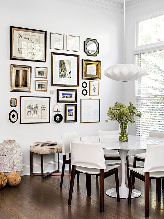 an elegant dining room with a round table and creamy chairs, a pendant lamp and a chic free form gallery wall