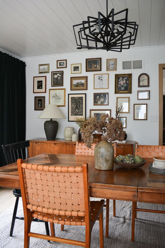 an elegant dining room with rich-stained furniture and leather woven chairs, a black chandelier and a catchy vintage gallery wall