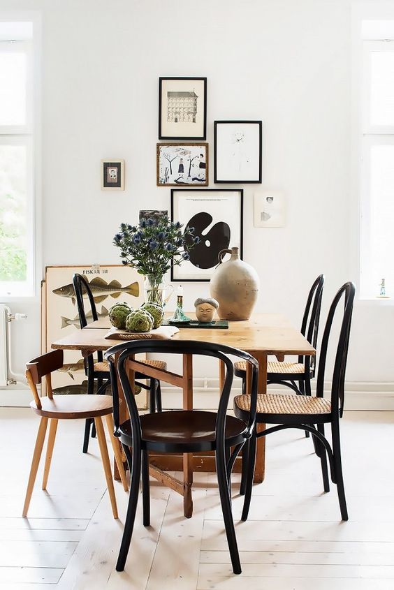 an elegant mid-century modern dining room with a stained table and mismatching chairs, a chic free form gallery wall and some decor
