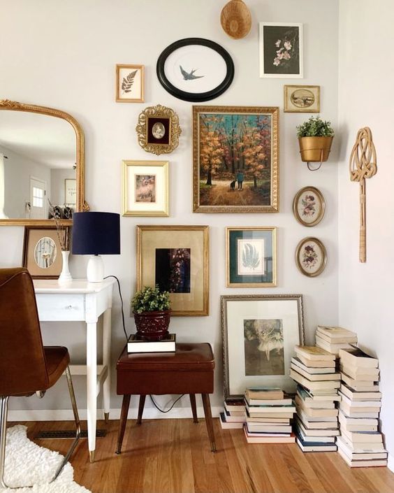 an elegant vintage home office with a white desk, a brown chair and a side table, a vintage gallery wall and a mirror plus stacks of books