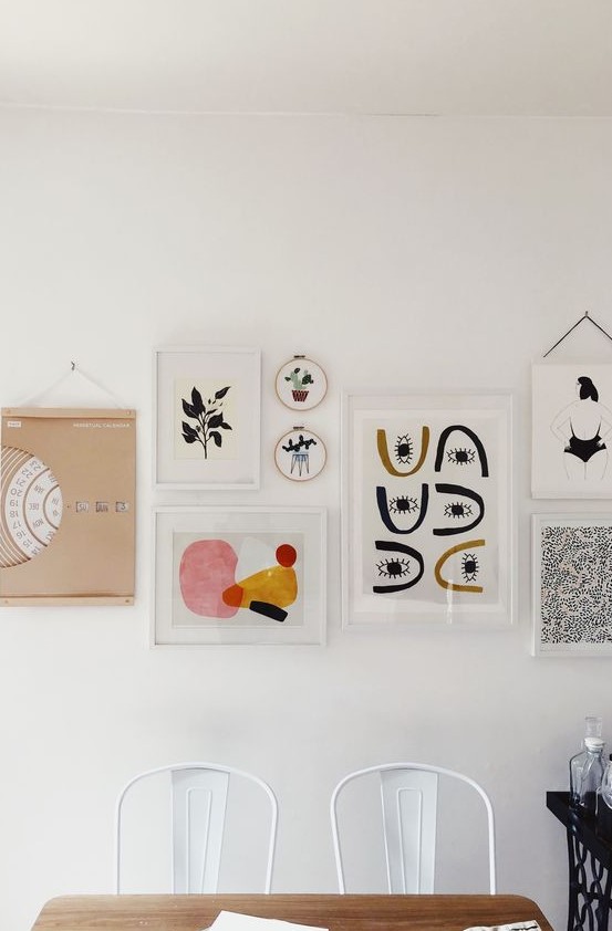 an eye-catchy gallery wall with white and blonde wood frames, with bold graphic artworks is chic and cool