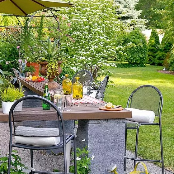 an outdoor cooking and dining space with a concrete and wood corner table and metal stools is a lovely and comfy space