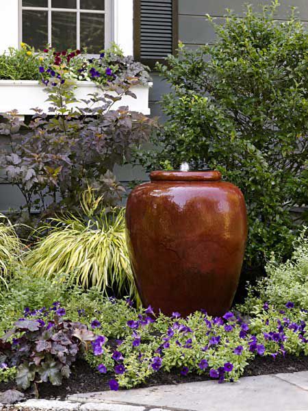 bright blooms and greenery plus an amphora fountain are a gerat and chic idea for a low maintenance front yard