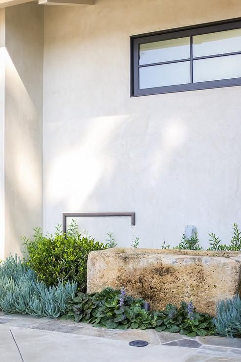 pretty greenery, succulents and a modern version of a fountain, a stone tub with a metal faucet for a modern front yard