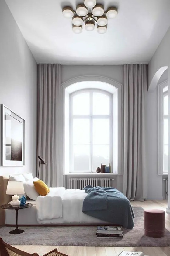 a modern bedroom with a double-height ceiling, an arched window done with grey curtains hanging under the ceiling to accent this height