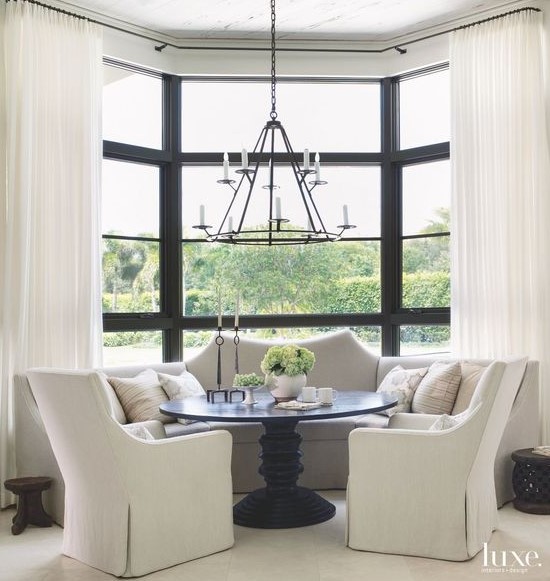 a monochromatic dining space with a large bow window done with semi sheer draperies that match the color scheme and make the space cozier