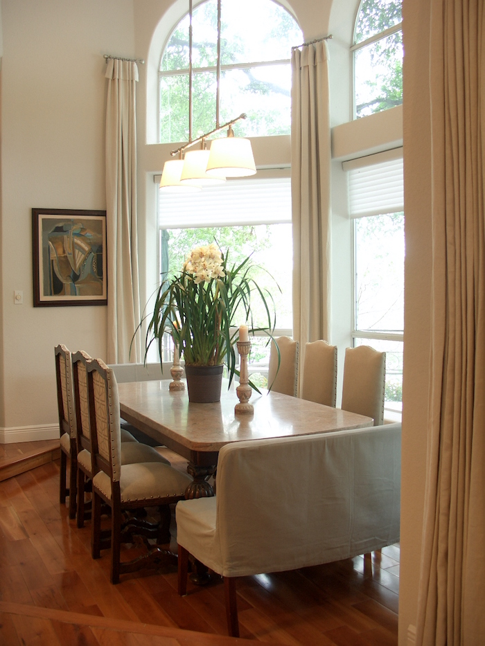 a neutral dining room with tall windows with arched tops and neutral curtains that cover the windows partly