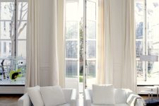 23 a sophisticated white living room with high ceilings, arched French windows, each of them done with creamy drapes that match