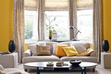 32 a bright grey and yellow living room with a bow window done with printed curtains, grey seating furniture and a refined table