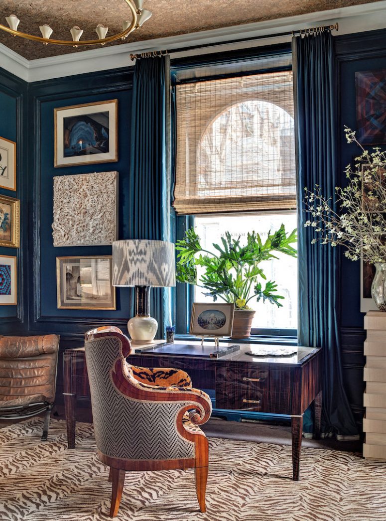 a refined blue home office with navy walls, an arched window covered with blinds and navy curtains additionally, chic vintage furniture and decor