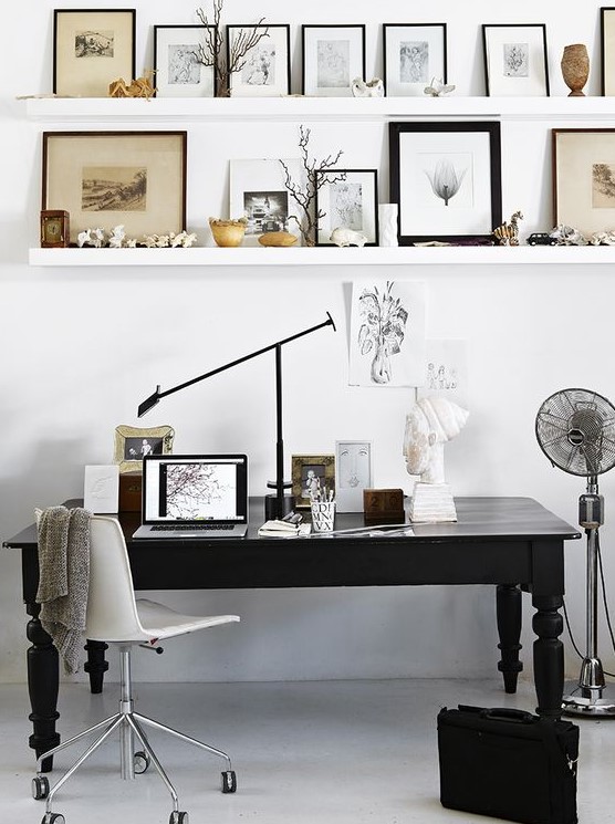 a Scandinavian home office with floating shelves, a black vintage desk, a white chair, a beautiful gallery wall and a fan