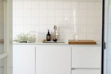a Scandinavian kitchen in white, with a stacked square tile backsplash and an open shelf over the cabinets