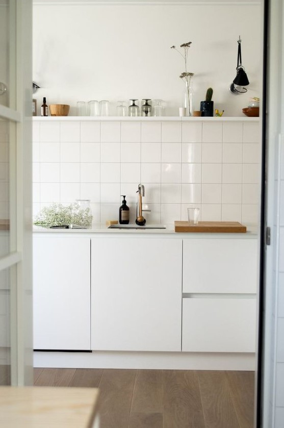 a Scandinavian kitchen in white, with a stacked square tile backsplash and an open shelf over the cabinets