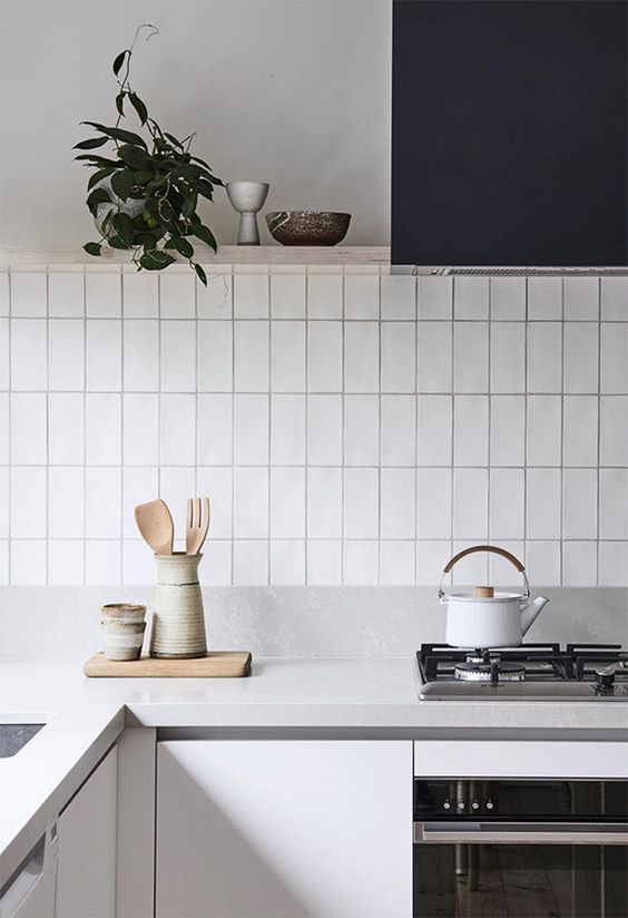 a Scandinavian kitchen with sleek white cabinets, a black hood, a white stacked tile backsplash and neutral stone countertops