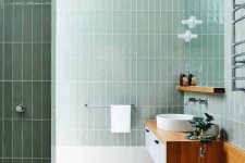 a bathroom clad with mint skinny stacked tiles, white terrazzo tiles on the floor, a floating vanity with a built-in bench