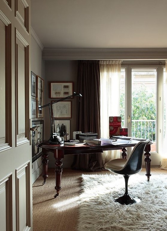 a beautiful dove grey home office with a monchromatic gallery wall, a dark stained desk and a pretty chair plus a table lamp