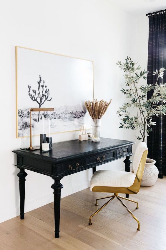 a beautiful home office with a vintage black desk, a modern gold and white chair, a statement artwork and a potted plant