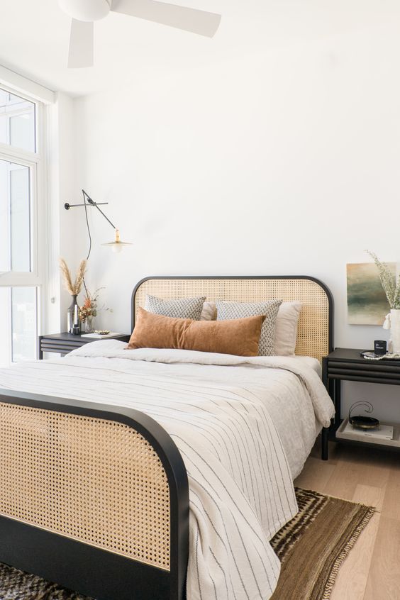 a beautiful mid-century modern bedroom with a bed with a cane headboard and foot, black nightstands and a sconce