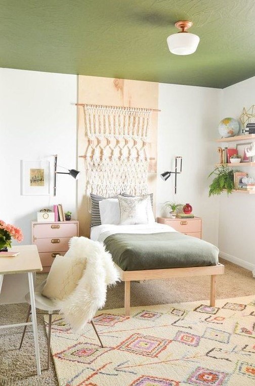 a boho teen room with a green ceiling, a macrame hanging, floating shelves, pink nightstands and a tiny desk and a chair