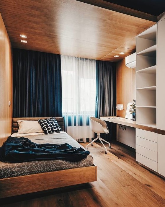 a bold minimalist teen room with a wooden ceiling with lights, navy curtains, a storage unit with a built-in desk, a comfy bed and blue bedding