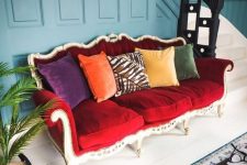 a bright eclectic entryway finished off with a bold vintage red sofa and colorful pillows