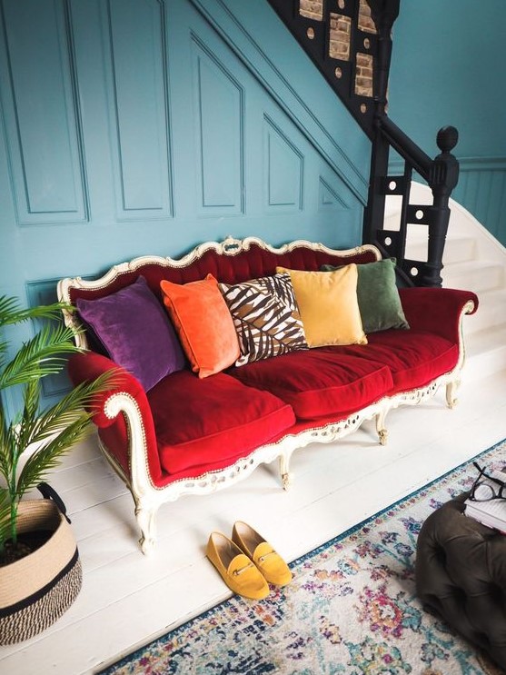 a bright eclectic entryway finished off with a bold vintage red sofa and colorful pillows