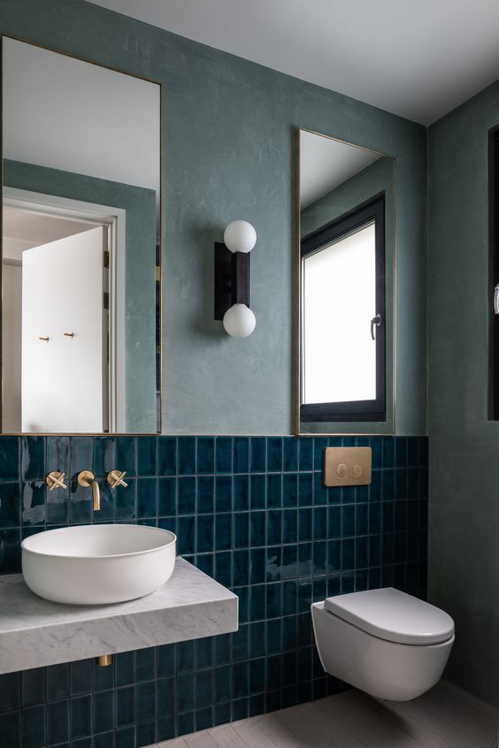a catchy mint-colored bathroom with navy stacked tiles, two mirrors, a floating vanity and a round sink and a window for natural light